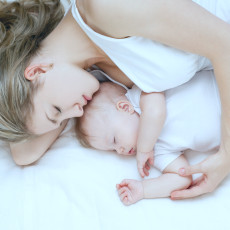 Mutter und Baby liegen auf dem Bett, die Mutter hält das Baby im Arm