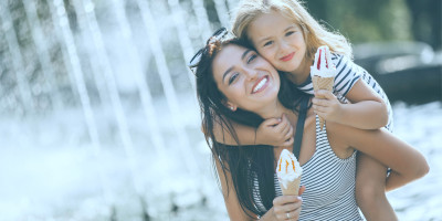 Mutter hat Tochter auf dem Rücken, beide essen ein Eis