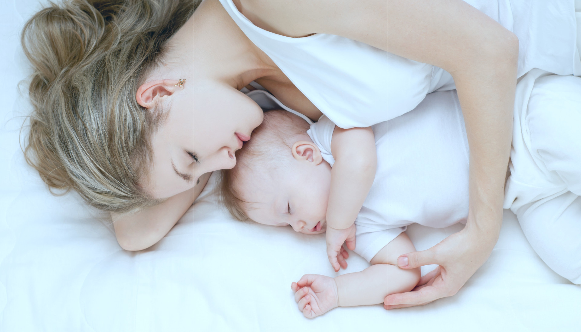 Mutter und Baby liegen auf dem Bett, die Mutter hält das Baby im Arm