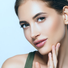 Frau lächelt in die Kamera und fasst sich mit den Fingerspitzen an ihr Gesicht