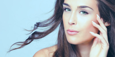 Frau mit langen braunen Haaren und grünen Augen schaut in die Kamera hält ihre Hand an die Wange