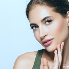 Frau neigt den Kopf, lächelt in die Kamera, hält ihr Kinn